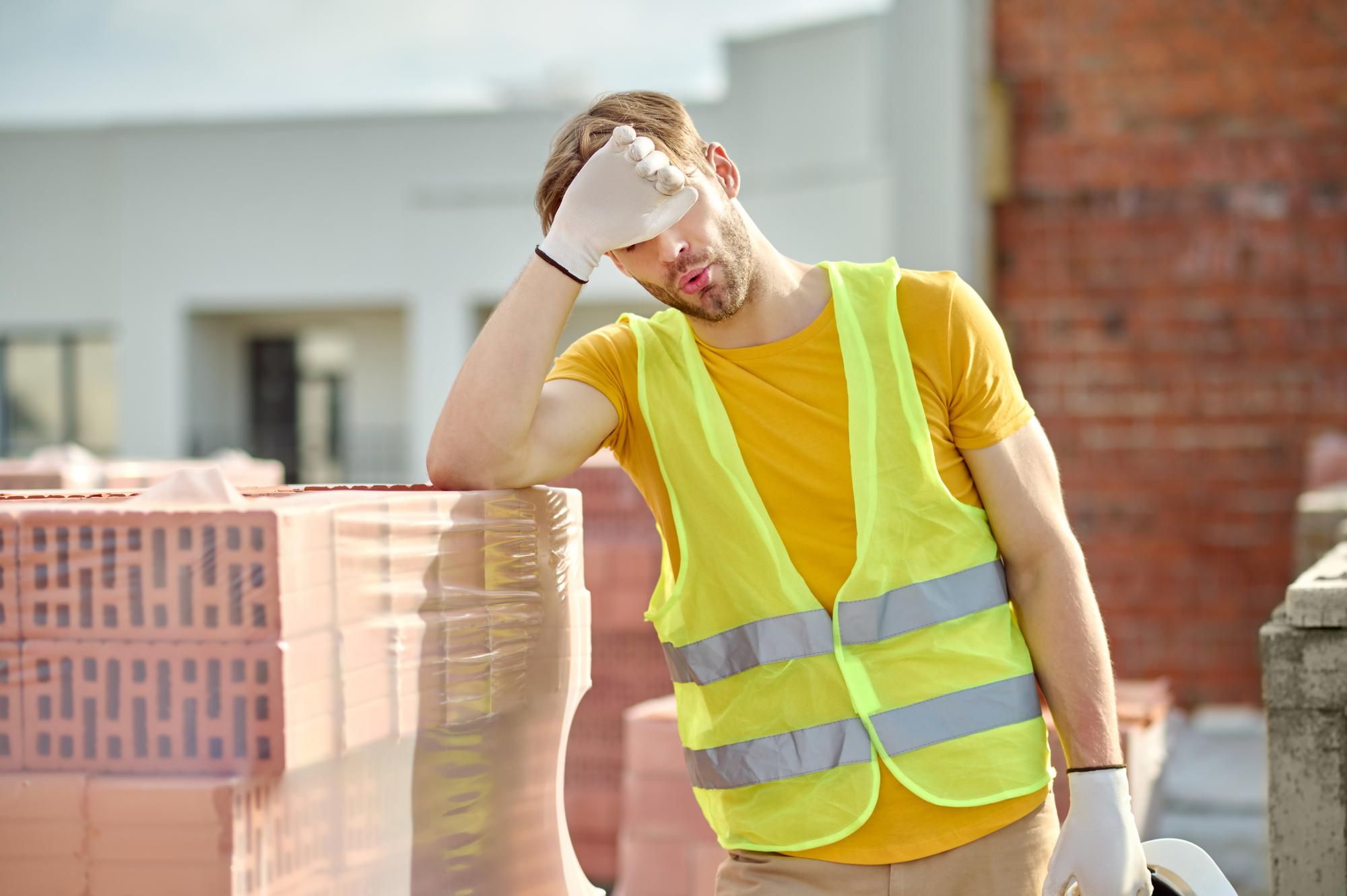 Un ouvrier épuisé sur un chantier s'essuie le front d'un revers de la main.