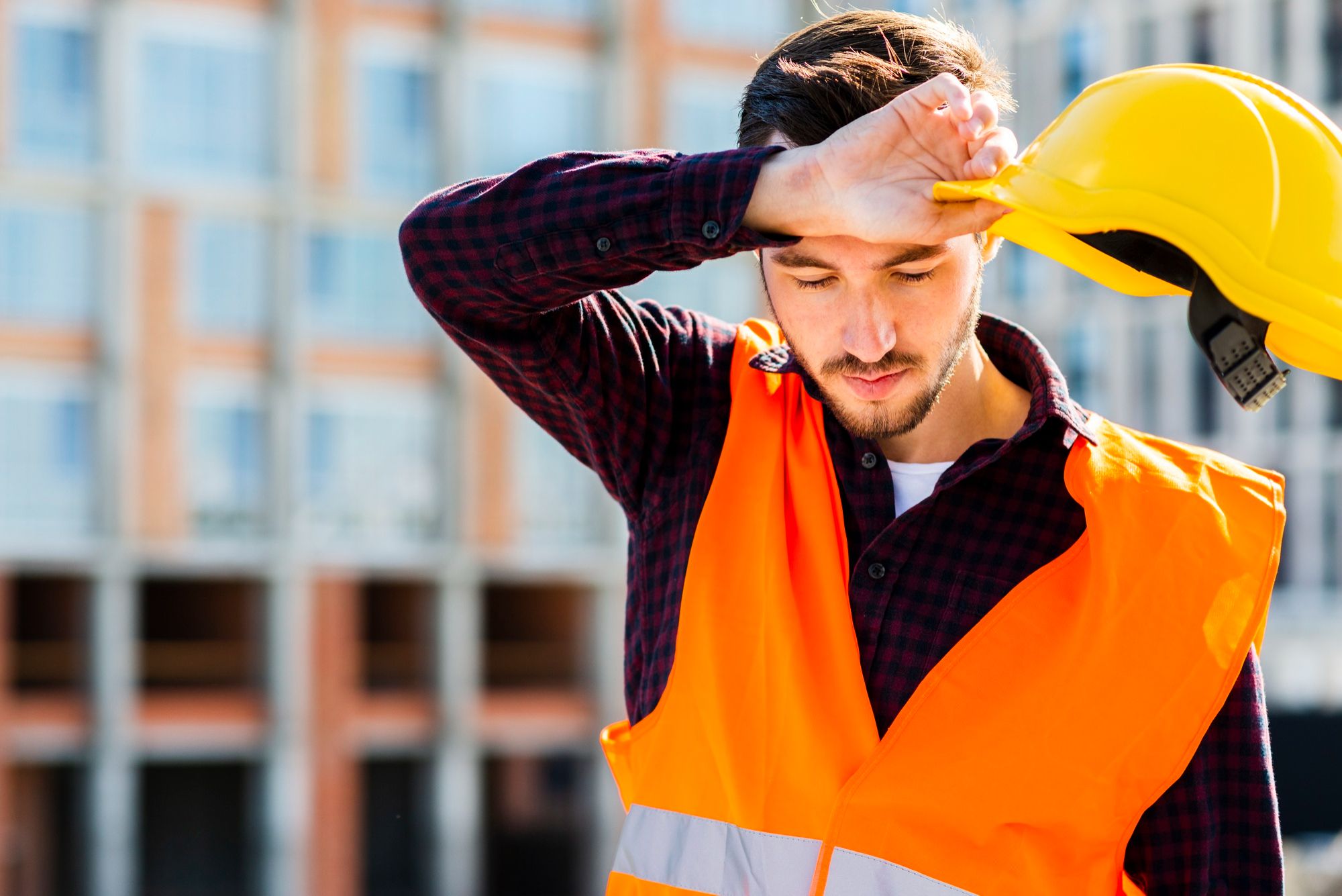 Un ouvrier du bâtiment fatigué retire son casque de chantier pour s'essuyer le front.
